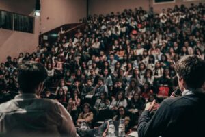 Spreker voert nagesprek met publiek in een volle theaterzaal