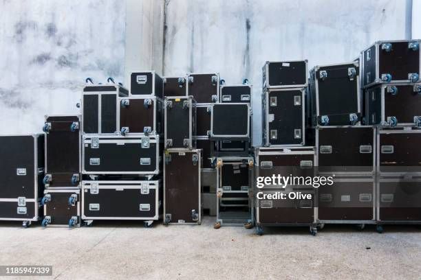 Een grote verzameling zwarte flightcases met wielen gestapeld tegen een muur.